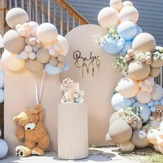 a teddy bear sitting in front of a cake and balloon arch with balloons on it