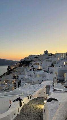 the sun is setting over some white buildings in oia, with water and mountains in the background