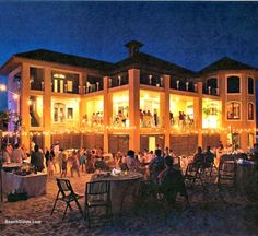 a group of people sitting at tables in front of a large building with lights on it