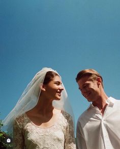 a man and woman standing next to each other in front of a blue cloudy sky