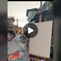 a man is painting on an easel in front of a building and holding a frisbee