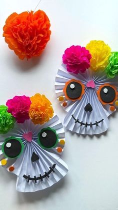 two paper fans decorated with colorful flowers and skull face decorations on a white table next to a red heart