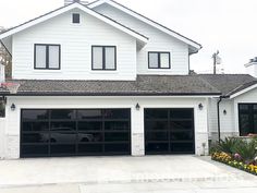 a car is parked in front of a two story white house with black garage doors