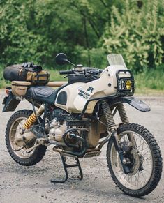 a dirt bike parked on top of a gravel road next to trees and bushes in the background