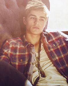 a young man sitting in a chair wearing a plaid shirt