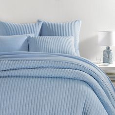 a bed with blue comforters and pillows in a white room next to a lamp