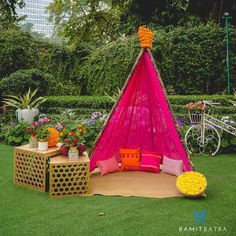 a pink and yellow tent sitting in the middle of a lush green field next to flowers