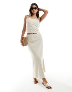 a woman in a white top and skirt posing for the camera with her hand on her head