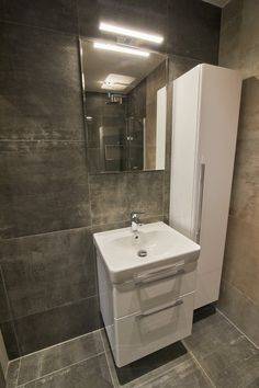 a white sink sitting next to a tall mirror in a bathroom on top of a tiled floor