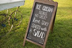 a chalkboard sign sitting in the grass next to a wagon with writing on it