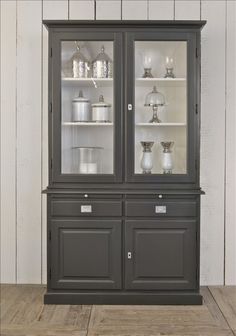 an old china cabinet with glass doors and shelves on each side, in front of a white wall