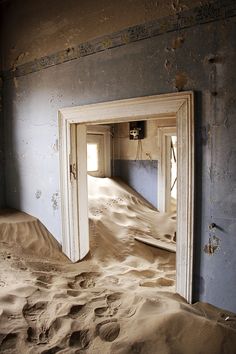 an open door in the middle of a room with sand on the floor and walls