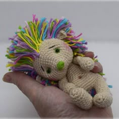 a hand holding a small crocheted stuffed animal with multicolored manes