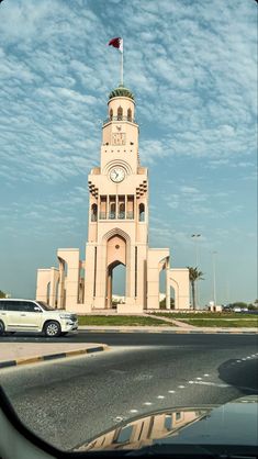 a car is parked in front of a large building with a clock on it's tower