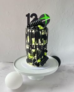 a black and white cake on a plate with green decorations around the top that reads'13th birthday '