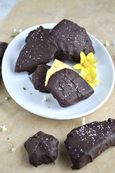 pieces of chocolate on a white plate next to a yellow flower