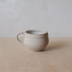 a white ceramic cup sitting on top of a wooden table next to a concrete wall