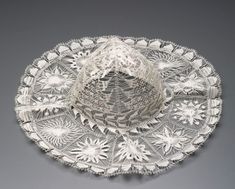 an intricately designed hat is shown on a gray surface, with white flowers in the center