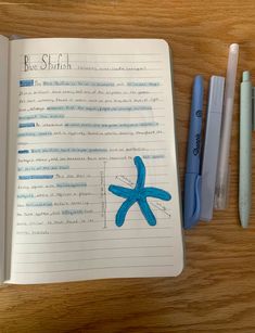 an open notebook with blue starfish drawn on it next to two markers and a pen