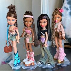 four bratz dolls are lined up next to each other on a table in front of a mirror