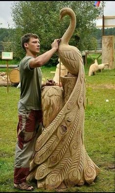 a man standing next to a carved peacock on top of a green grass covered field