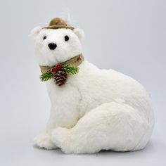 a stuffed polar bear wearing a hat and holding a pine cone in its mouth, sitting on the ground