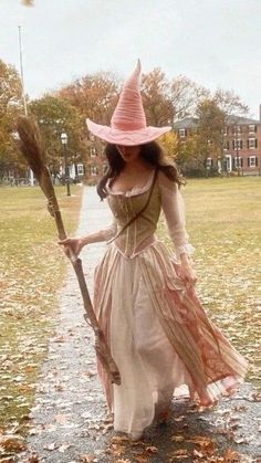 a woman in a long dress and hat holding a broom while walking down a path