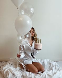 a woman sitting on top of a bed holding a cake with candles in her hands