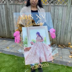 a woman holding up a photo in front of a fence with pink gloves on her hands