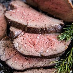 sliced steak with rosemary sprig on the side, served on a black plate