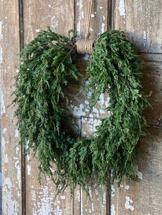 a green wreath hanging on the side of a wooden door next to a string and rope