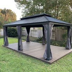 a gazebo in the middle of a yard with curtains on it's sides