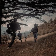 three people are running up a hill in the dark with trees and mountains behind them