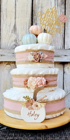 there is a multi layer cake with flowers on the top and two small pumpkins in the middle