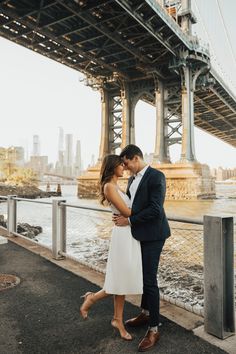 a man and woman are standing under the bridge by the water in their wedding attire