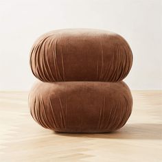 two brown pillows sitting on top of each other in front of a white wall and wooden floor