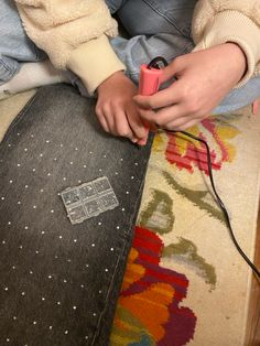 a person sitting on top of a rug with a pink object in their hand next to it