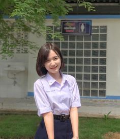 a woman standing in front of a building wearing a purple shirt and blue skirt with her hands on her hips