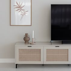 a flat screen tv sitting on top of a wooden cabinet next to a vase and candle