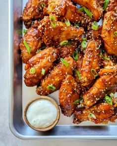 chicken wings with sesame seeds and green onions on a tray next to a small bowl of ranch dressing