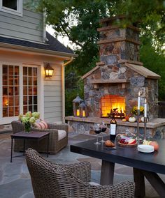 an outdoor fireplace with wicker chairs around it and a table on the patio next to it