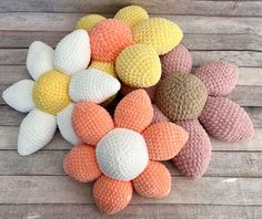 several knitted flowers sitting on top of a wooden table with white and yellow ones