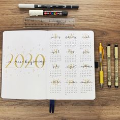 an open planner with markers, pencils and marker pens next to it on a wooden table