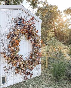 a wreath is hanging on the side of a white building with trees in the background