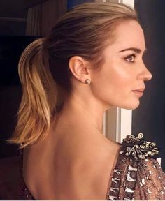 a woman with blonde hair wearing a gold dress and earrings, looking out the window