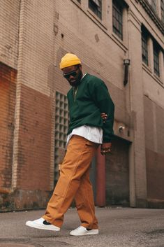 a man in green jacket and yellow hat walking on street next to brick building with white shoes