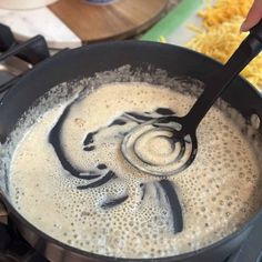 a person is stirring something in a pan on the stove with a black spatula