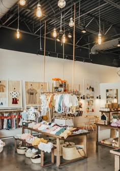 the inside of a clothing store with lots of items on tables and lamps hanging from the ceiling