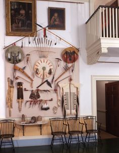 a wall with several pieces of art hanging from it's sides and two chairs sitting in front of them