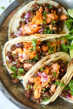 three tacos on a plate with lime wedges